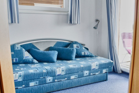 Blue bedroom with a modern sofa, large pillows, and striped curtains on a houseboat in Germany.