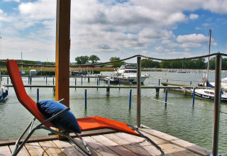 En afslappende liggestol på en husbåd med udsigt over en marina med både under en delvist overskyet himmel.