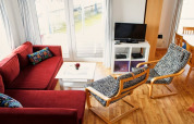 Sala de estar en una casa flotante con sofá rojo, sillas estampadas, TV, mesa blanca y vista al agua.