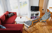 Houseboat living room with red sectional sofa, patterned chairs, TV, white coffee table, and water view.