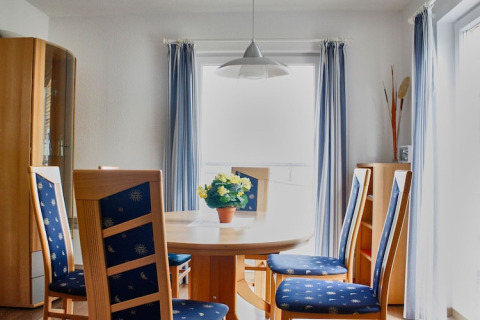 Sala da pranzo su una casa galleggiante con tavolo rotondo, sedie blu e tende leggere alle finestre.