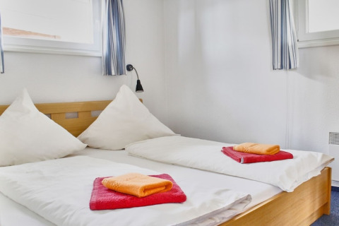 Slaapkamer op een woonboot met twee enkele bedden, witte dekbedden en felgekleurde handdoeken.
