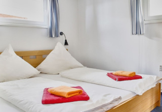 Camera da letto su una houseboat con due letti singoli, piumini bianchi e asciugamani colorati.