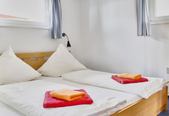 Bedroom on a houseboat featuring two single beds with white duvets and colorful towels on top.