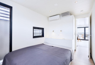 Camera moderna sulla houseboat Fjordblick in Germania con letto matrimoniale, finestra e pareti bianche.
