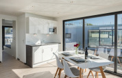 Interior de una moderna casa flotante con mesa comedor, cocina y grandes ventanales con vista al puerto.