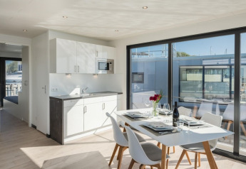 Modern woonbootinterieur met eettafel, keukenblok en grote ramen met uitzicht op de haven en boten.