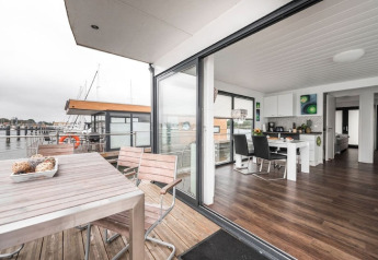 Moderne woonboot met open keuken, eetruimte en terras met zicht op de haven en aangemeerde boten.