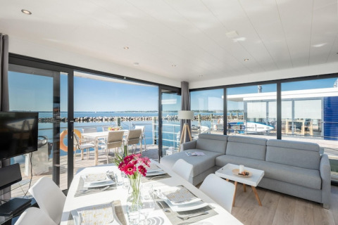 Luminoso y moderno salón en una casa flotante con vistas panorámicas al agua y terraza soleada exterior.