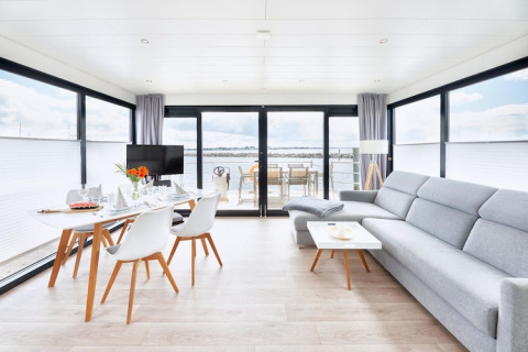 Intérieur moderne et lumineux d'une péniche avec grandes baies vitrées, table à manger et vue sur l'eau.