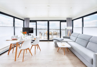 Intérieur moderne et lumineux d'une péniche avec grandes baies vitrées, table à manger et vue sur l'eau.