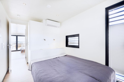 Chambre lumineuse sur une péniche avec lit double, climatisation, fenêtres modernes et décoration épurée.