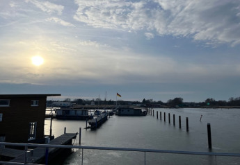 Casa flotante en un puerto tranquilo al amanecer con pilotes y cielo parcialmente nublado y soleado.