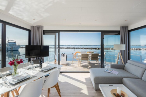 Moderne husbåd 'Fjordblick' i Tyskland med spisebord, stue og terrasse med udsigt over fjorden.