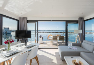 Houseboat moderno 'Fjordblick' in Germania con zona pranzo, salotto e terrazza vista acqua.