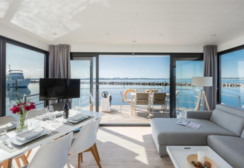 Casa flotante moderna 'Fjordblick' en Alemania, con comedor, sala y terraza con vista al agua.