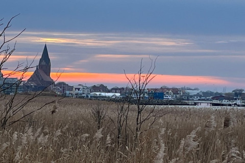 Uitzicht over een veld naar een dorp met kerktoren bij zonsondergang, vanaf Houseboat Fjordblick in Duitsland.