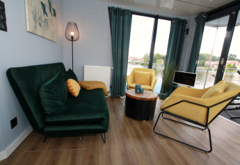 Living room on Houseboat Friedrich in Germany with green sofa, yellow chairs, and waterfront windows.