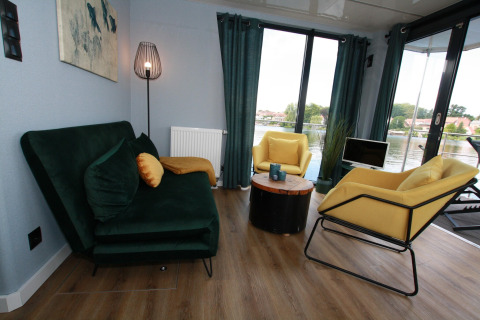 Woonkamer op Houseboat Friedrich in Duitsland met groene zetel, gele stoelen en uitzicht op het water.