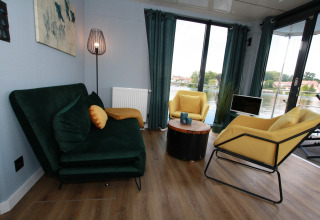 Woonkamer op Houseboat Friedrich in Duitsland met groene zetel, gele stoelen en uitzicht op het water.