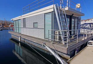 Casa flotante moderna atracada junto al muelle bajo un cielo azul, Houseboat Family & Friends LP2, Alemania.