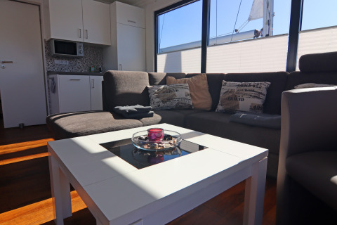 Lyst og moderne stue på husbåden 'Family & Friends LP2' i Tyskland med sofa og køkkenområde.