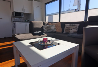 Stue på husbåden Family & Friends LP2 med moderne sofa, køkken og stort vindue i Tyskland.