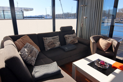 Soggiorno sulla Houseboat Family & Friends LP2 in Germania con divano, poltrona e vista sull'acqua.
