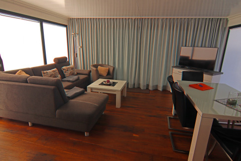Woonkamer op woonboot Family & Friends LP2 met moderne stijl, grijze zetel, tv en grote ramen in Duitsland.