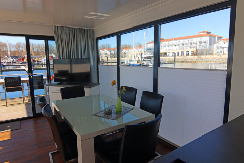 Zona giorno moderna di una houseboat con grandi finestre e vista sul porto turistico in Germania.