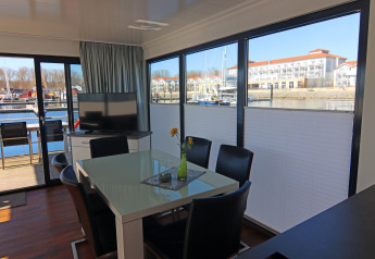 Moderne leefruimte op woonboot met grote ramen en zicht op jachthaven in Duitsland, tafel en TV.