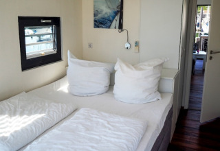 Slaapkamer in een woonboot met een tweepersoonsbed, grote witte kussens en zicht op de jachthaven.