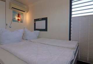 Camera da letto con letto matrimoniale, biancheria bianca, climatizzatore e quadro di faro sul muro.