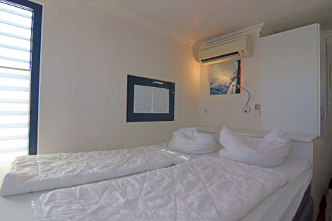 Slaapkamer met twee enkele bedden, witte lakens, raam, airco en moderne, eenvoudige inrichting.