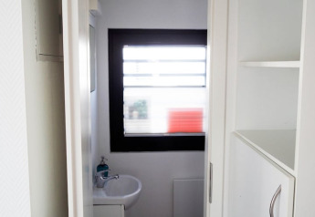 Kleine lavabo met raam en schappen op een woonboot, minimalistisch ingericht met veel daglicht.