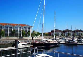 Moderne husbåde og sejlbåde fortøjet i havnen foran lejlighedsbygninger i Tyskland på en solskinsdag.