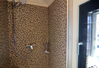 Moderne bruser med små mosaikfliser og glasvæg i et badeværelse på husbåden Family & Friends i Tyskland.