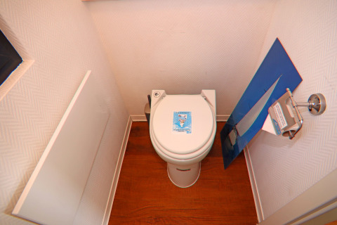 Et lille badeværelse på husbåd med et toilet, trægulv og vægkunst med sejlbådmotiv, Tyskland.