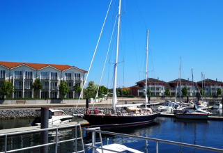 Woonboot 'Family & Friends LP2', aangemeerd in een jachthaven in Duitsland met moderne appartementen op de achtergrond.