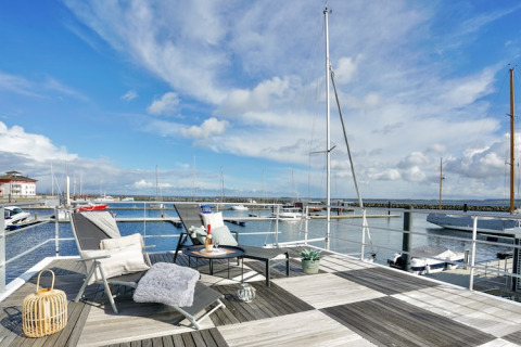 Terrasse de péniche avec chaises longues, table basse et vue sur le port et les voiliers.