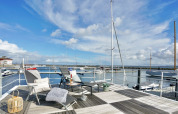 Woonbootterras met ligstoelen en tafel, uitkijkend over de jachthaven en aangemeerde zeilboten.