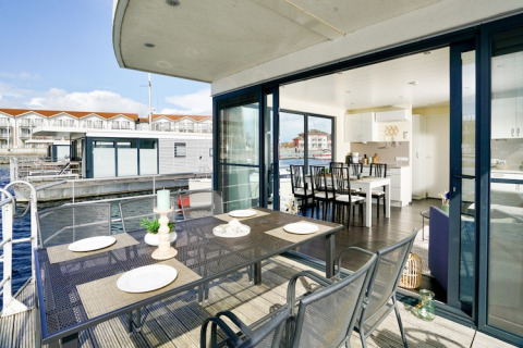 Houseboat moderna con tavolo da pranzo esterno, grandi vetrate e vista sull’acqua e altre houseboat.