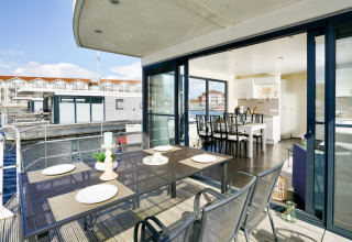 Moderne woonboot met terras en eettafel, schuifdeuren en zicht op het water en andere woonboten.