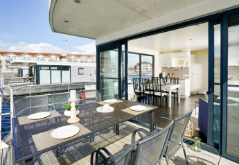 Modern houseboat with outdoor dining table, open sliding doors, and waterfront views of other houseboats.