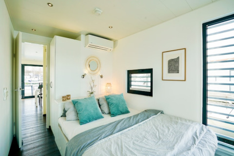 Modern slaapvertrek op een woonboot met grote ramen, gezellig bed en lichte, eigentijdse inrichting.