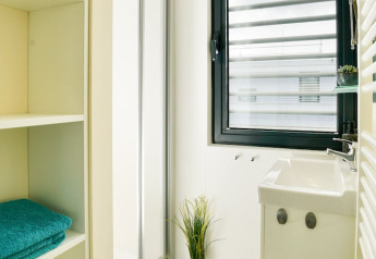 Lichte moderne badkamer op een woonboot met open kast, raam, kleine wastafel en decoratieve plant.