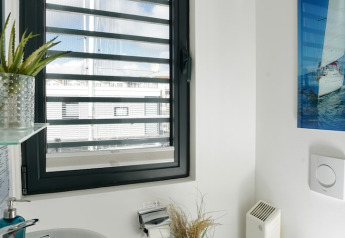 Badkamer op een woonboot met groot raam, groene plant, zeilboot-afbeelding en moderne witte muren.