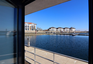 Vista da una houseboat in Germania con banchine, edifici moderni e un cielo sereno e azzurro.