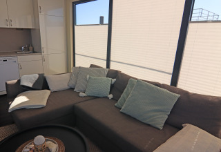 Cozy living area on a houseboat with a gray sofa, soft pillows, blankets, and large window blinds.