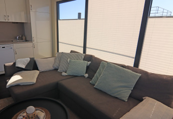 Cozy living area on a houseboat with a gray sofa, soft pillows, blankets, and large window blinds.